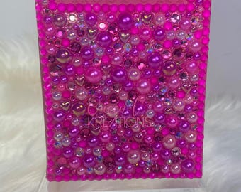 May include: A pink passport cover decorated with pink, purple and white pearls and rhinestones. The word "PASSPORT" is embossed on the cover.