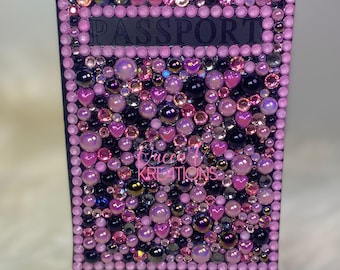 May include: A black passport cover with a pink border and a pink, black, and iridescent rhinestone design. The word "PASSPORT" is written in black on the cover.