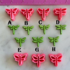 May include: A set of 9 dragonfly cookie cutters, 3 pink and 6 green. The green cutters have white dots. The cutters are labeled A through H.