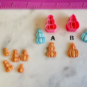 May include: Two pink plastic pumpkin cookie cutters, labeled A and B, with several small orange and blue pumpkin-shaped decorations.
