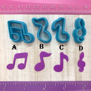 May include: Four blue plastic cookie cutters shaped like musical notes. The cutters are labeled A, B, C, and D. Below the cutters are four purple plastic cookie cutters shaped like musical notes.