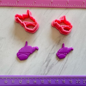 May include: Two sets of West Virginia state cookie cutters. One set is pink and the other is purple. The pink cutters are larger than the purple cutters. The cutters are made of plastic and have a bridge design.