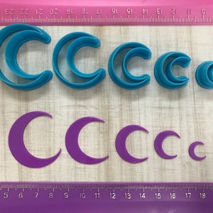 May include: Set of six blue plastic crescent moon cookie cutters and six purple plastic crescent moon cookie cutters of varying sizes.