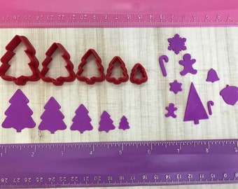 May include: A set of red plastic Christmas tree cookie cutters and purple fondant cutouts of Christmas trees, snowflakes, candy canes, bells, a gingerbread person, and an acorn.