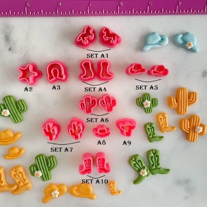 May include: A set of 10 cookie cutters in various shapes, including cowboy boots, cacti, hats, stars, and horseshoes. The cutters are pink, green, yellow, and blue. The cutters are labeled with the letters A1 through A10.