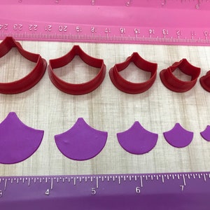 May include: Set of seven red and purple plastic cookie cutters shaped like a fan. The cutters are arranged in order of size from largest to smallest. A ruler is visible in the background.