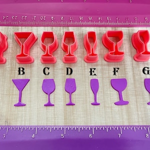 May include: Seven different pink plastic cookie cutters shaped like wine glasses. The cutters are labeled A through G.