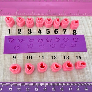 May include: A set of 14 pink silicone molds for baking. The molds are numbered 1 through 14. The molds are shaped like animals, butterflies, and other designs.