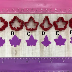 May include: Six red plastic leaf-shaped cookie cutters and six purple fondant leaf shapes. The cutters are labeled A through F. The fondant shapes are arranged in a row below the cutters.