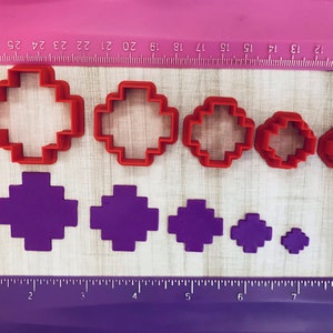 May include: Set of eight red and purple plastic cookie cutters shaped like a cross. The cutters are arranged in order of size, with the largest cutter at the top and the smallest cutter at the bottom.