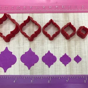 May include: Set of six red plastic cookie cutters in various sizes, shaped like a quatrefoil, with a purple fondant cutout of the same shape in the background.