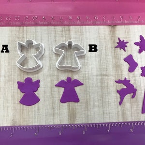 May include: Two white plastic angel cookie cutters, one with wings spread and one with wings folded, labeled A and B. Below them are two purple angel shapes, one with wings spread and one with wings folded. On the right side of the image are various purple Christmas cookie cutters, including a snowflake, a reindeer, a stocking, a gingerbread man, a tree, and a bell.