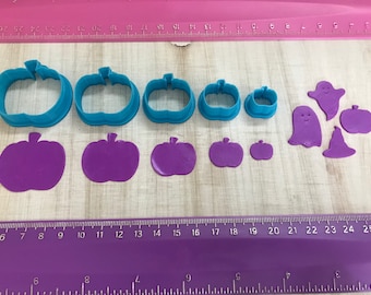 May include: A set of nine blue and purple plastic cookie cutters in the shapes of pumpkins and ghosts. The cutters are arranged on a purple and white ruler.