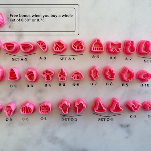 May include: A set of 10 pink plastic cookie cutters featuring various holiday and Halloween themes. The cutters are arranged in rows and labeled with letters and numbers. The text "Free bonus when you buy a whole set of 0.50" or 0.75" is at the top of the image.