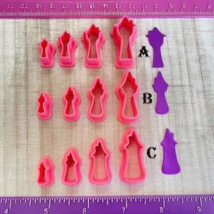 May include: A set of ten pink plastic cookie cutters shaped like different sized towers. The cutters are arranged in rows on a wooden surface with a ruler underneath. The ruler is marked in inches.