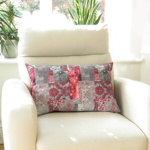 May include: A red and grey patterned lumbar cushion on a white armchair. The cushion has a patchwork design with geometric shapes and floral patterns.