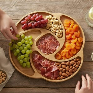 Può includere: Un vassoio di legno pieno di uva, anacardi, albicocche secche, mandorle e carne a fette. Sono presenti anche un bicchiere d'acqua con fette di limone e una ciotolina.