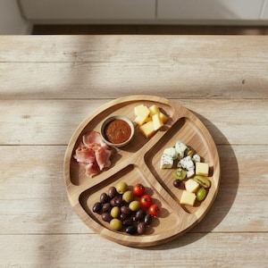 Könnte beinhalten: Ein runder Servierteller aus Holz mit vier Fächern, gefüllt mit verschiedenen Vorspeisen. Enthält Prosciutto, Oliven, Käse und eine kleine Schüssel mit Sauce. Der Teller liegt auf einer hellen Holzoberfläche.