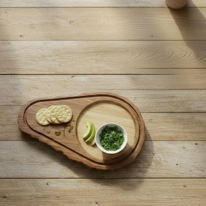 Puede incluir: Tabla de servir de madera con borde natural, con galletas saladas, rodajas de aguacate y un cuenco pequeño con salsa verde. La tabla está sobre una superficie de madera clara.