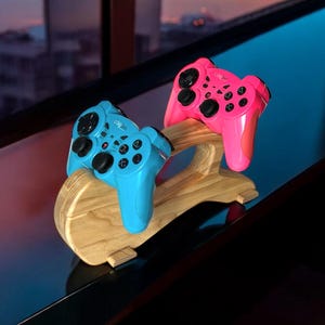 May include: A wooden stand with two video game controllers, one blue and one pink.