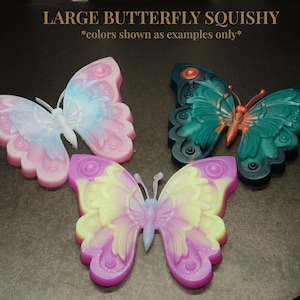 May include: Three large butterfly-shaped squishy toys. One is pink and white, one is green and orange, and one is purple and yellow. *colors shown as examples only*