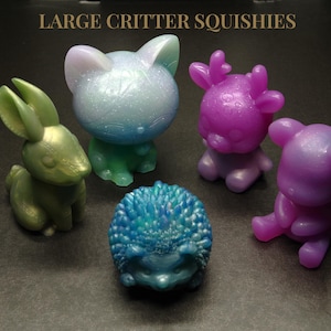 May include: Five colorful, squishy toys in the shape of a cat, deer, rabbit, hedgehog, and bear. The toys are made of a soft, flexible material and have a sparkly finish.  The toys are all different colors, including green, purple, blue, and white.