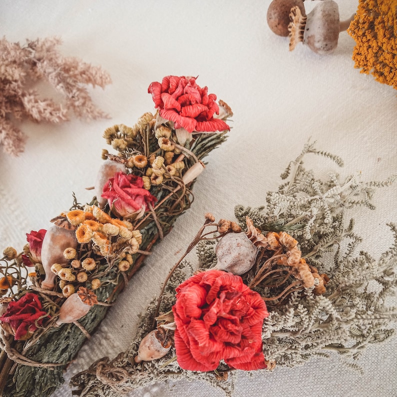 May include: Two bundles of dried flowers and herbs, tied together with twine. One bundle features red flowers and yellow flowers, while the other bundle features red flowers and gray-green herbs.