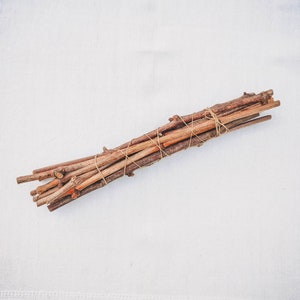 May include: A bundle of brown twigs tied together with twine, arranged on a white linen background.