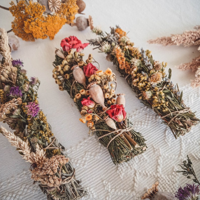 May include: Three bundles of dried herbs and flowers tied together with twine. The bundles are made with a variety of dried flowers and herbs, including lavender, poppy pods, and dried grasses. The bundles are a natural, earthy color.