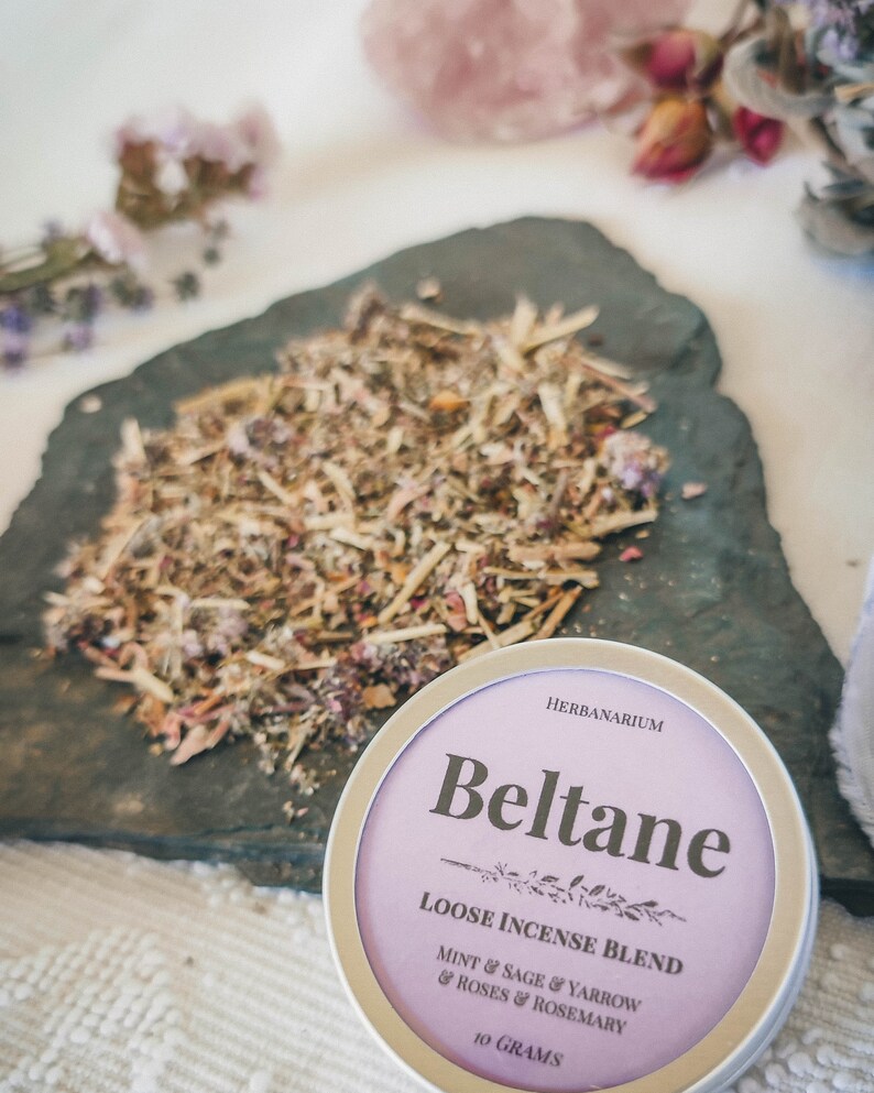 May include: A purple and silver tin of loose incense blend called "Beltane" with the text "HERBANARIUM" and "LOOSE INCENSE BLEND MINT & SAGE & YARROW & ROSES & ROSEMARY 10 GRAMS".