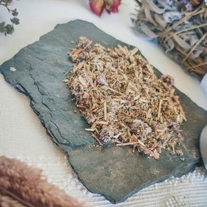 May include: A close-up of a slate tile with a mixture of dried herbs and flowers. The herbs and flowers are a mix of brown, green, and pink.