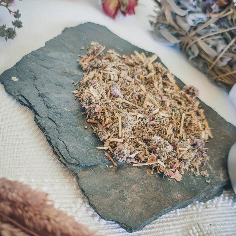 May include: A close-up of a slate tile with a mixture of dried herbs and flowers. The herbs and flowers are a mix of brown, green, and pink.