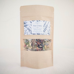 May include: A brown paper bag with a clear window showing a mix of dried herbs and spices. The bag has a white label that says "Shower Pot Time to Relax" and lists the ingredients: Eucalyptus, Sage, Chamomile, Rosemary, Juniper Berry, Rose, Hilibane, Lavender.