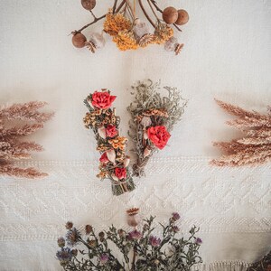 May include: Two bundles of dried flowers and herbs, one with red flowers and the other with white flowers, on a white background.