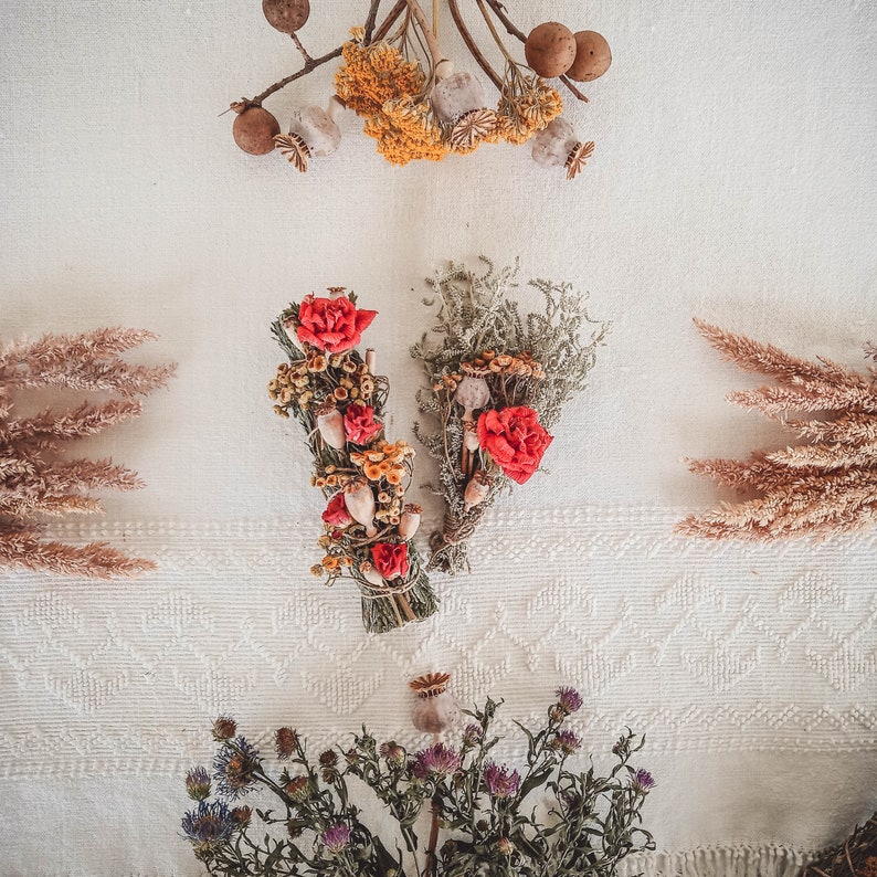 May include: Two bundles of dried flowers and herbs, one with red flowers and the other with white flowers, on a white background.