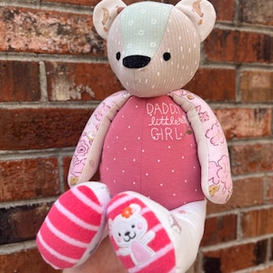 May include: A handmade teddy bear with a patchwork design. The bear has a pink body with white polka dots and the text "Daddy's Little Girl". The bear's ears and arms feature floral patterns. The bear's feet are pink and white striped.