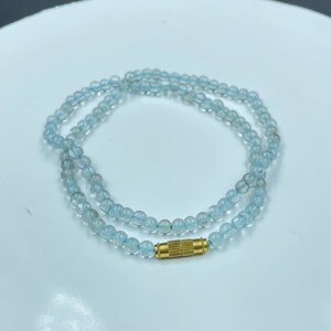 May include: A delicate necklace made of light blue aquamarine beads with a gold clasp.