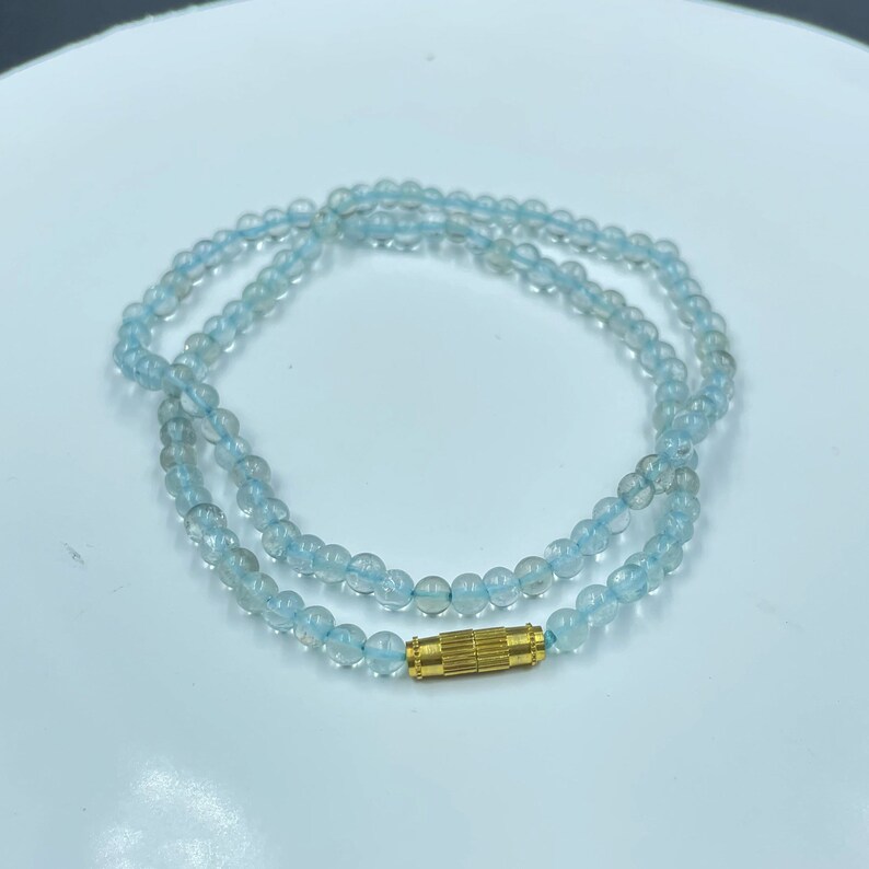 May include: A delicate necklace made of light blue aquamarine beads with a gold clasp.