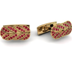 Può includere: Gemelli dorati con un design a forma di foglia, ciascuno ornato da numerose piccole gemme rosse rotonde. I gemelli sono presentati su uno sfondo bianco, mettendo in risalto i loro dettagli intricati e la finitura lucida.