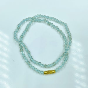 May include: A light blue gemstone necklace with a gold clasp. The necklace is made of round beads and is approximately 18 inches long.