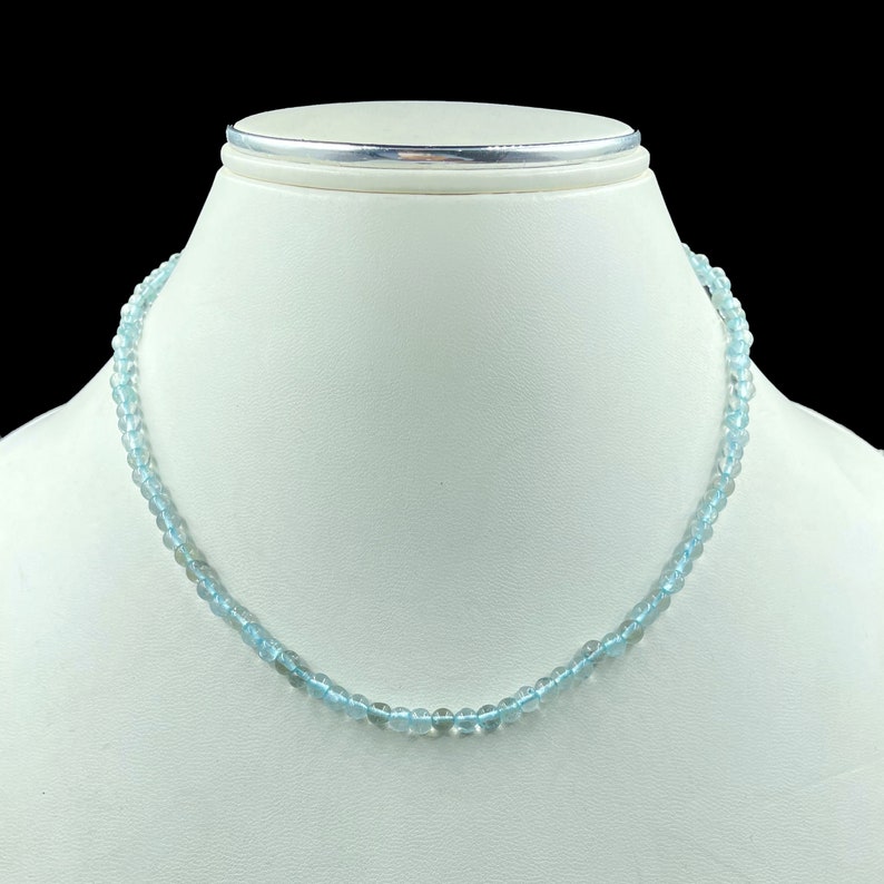 May include: A light blue gemstone necklace made of round beads. The necklace is on a white mannequin bust.