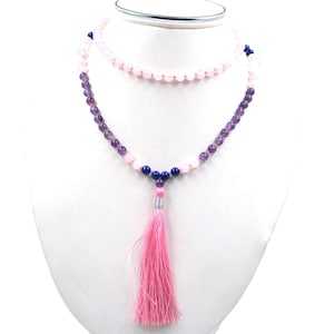 Könnte beinhalten: Halskette mit zwei Schichten aus Amethyst-, Rosenquarz- und blauen Perlen. Die untere Schicht hat eine rosa Quaste. Die Halskette wird auf einer weißen Schaufensterpuppe präsentiert. Die Perlen sind rund und die Quaste ist hellrosa.