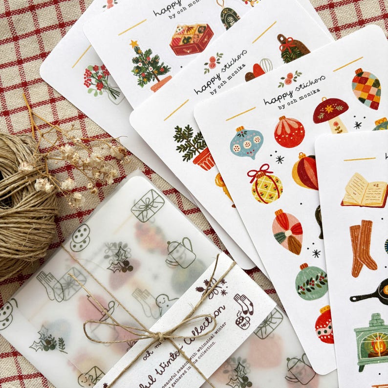 Może przedstawiać: Kolekcja naklejek i papieru prezentowego z zimowymi ilustracjami. Naklejki, oznaczone jako "happy stickers by och monika", przedstawiają świąteczne wzory, takie jak choinki i ozdoby. Papier prezentowy jest związany sznurkiem i zawiera podobną zimową grafikę.