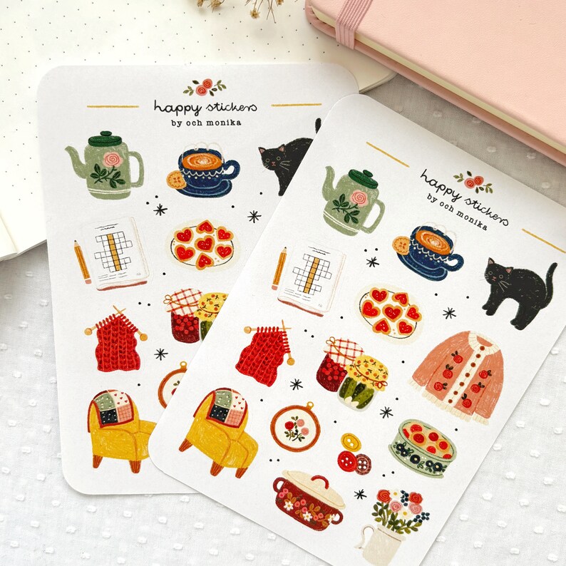 Op de afbeelding: Twee vellen met stickers met verschillende illustraties, waaronder een theepot, een kopje thee, een kat, een gebreide sjaal, een pot jam, een stoel, een kom met koekjes, een ovenschaal, een bloempot en een kruiswoordpuzzel. De stickers zijn gelabeld met "happy stickers by ooch monika".