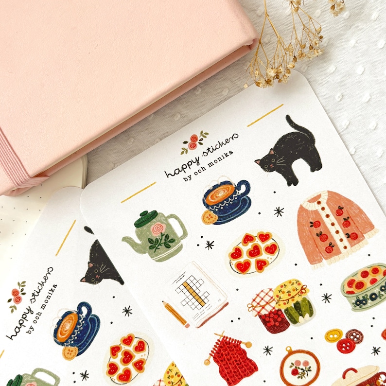 Op de afbeelding: Een vel stickers met illustraties van een theepot, een kopje thee, een kat, een trui, een bord met koekjes, een pot jam, een gebreide sjaal, een borduurring, een knoop en een kruiswoordpuzzel. De stickers zijn gelabeld "happy stickers by och monika".