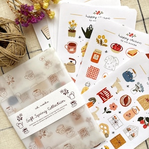 Könnte beinhalten: Eine Sammlung von Aufklebern zum Thema Frühling mit Illustrationen von Teekannen, Blumen und Lebensmitteln. Die Aufkleber sind in einer Klarsichtverpackung mit dem Text "Soft Spring Collection" und "happy stickers by och monika" verpackt.