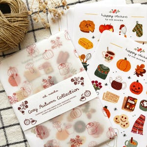 Può includere: Una collezione di adesivi a tema autunnale, tra cui zucche, teiere e foglie. Gli adesivi sono su carta bianca con il testo "happy stickers by ooh monika" e "Cozy Autumn Collection". La tavolozza dei colori include arancione, marrone e verde.
