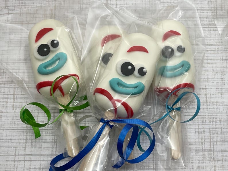 May include: Four white chocolate cake pops decorated with the face of the character 'Forky' from the movie Toy Story. Each cake pop is wrapped in clear plastic and tied with a ribbon.