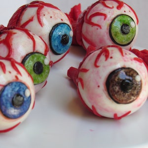 K&ouml;nnte beinhalten: F&uuml;nf realistisch aussehende Augenbonbon-Dekorationen mit roten Adern, wei&szlig;er Sklera und unterschiedlichfarbigen Iris. Die Augen sind aus Fondant und perfekt f&uuml;r Halloween-Partys oder gruselige Dekorationen.