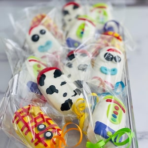 May include: A clear plastic container filled with colorful cake pops decorated with characters from the Toy Story movie franchise. The cake pops are on sticks and wrapped in clear plastic bags with colorful ribbons.